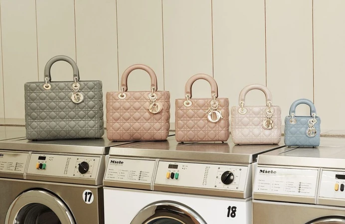 Five luxury quilted leather handbags with top handles arranged on top of stainless steel Miele washing machines in a laundry room setting.