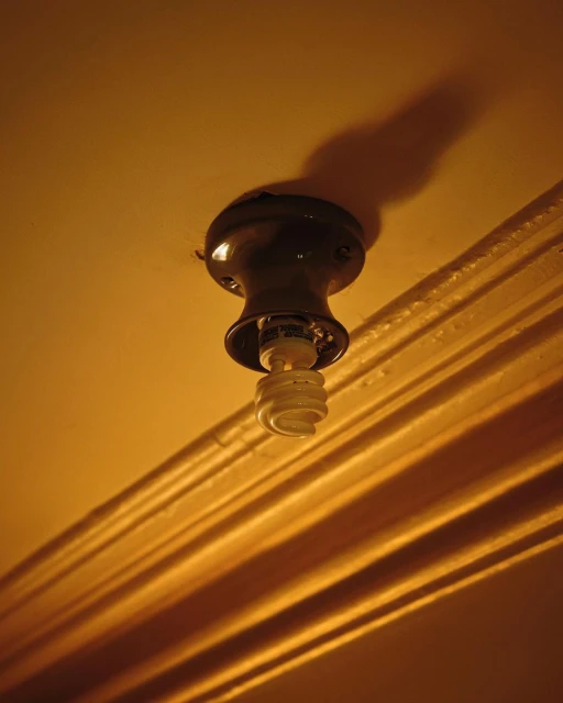Close-up of a compact fluorescent lamp (CFL) hanging from a black fixture on a yellow ceiling, casting shadows.