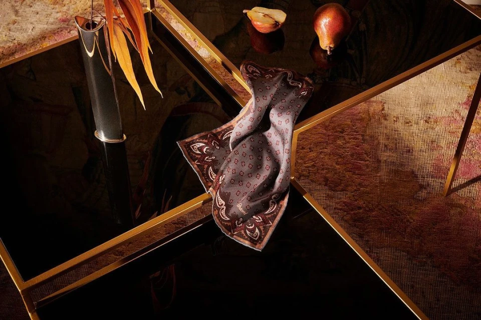 Still life featuring a folded paisley scarf, pears, and a black vase on a black and gold tiered coffee table, indoor, soft lighting.