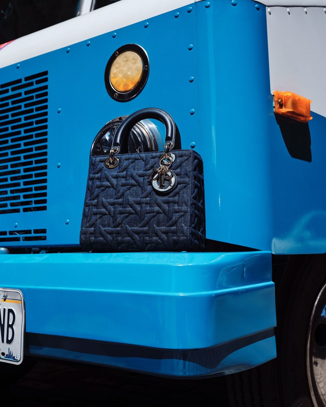 Denim Lady Dior handbag displayed on the bumper of a bright blue truck with white trim and a California license plate.
