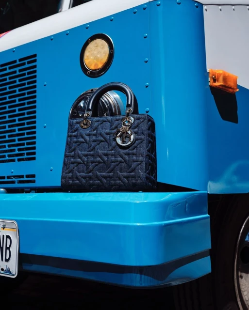 Denim Lady Dior handbag displayed on the bumper of a bright blue truck with white trim and a California license plate.