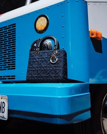Denim Lady Dior handbag displayed on the bumper of a bright blue truck with white trim and a California license plate.
