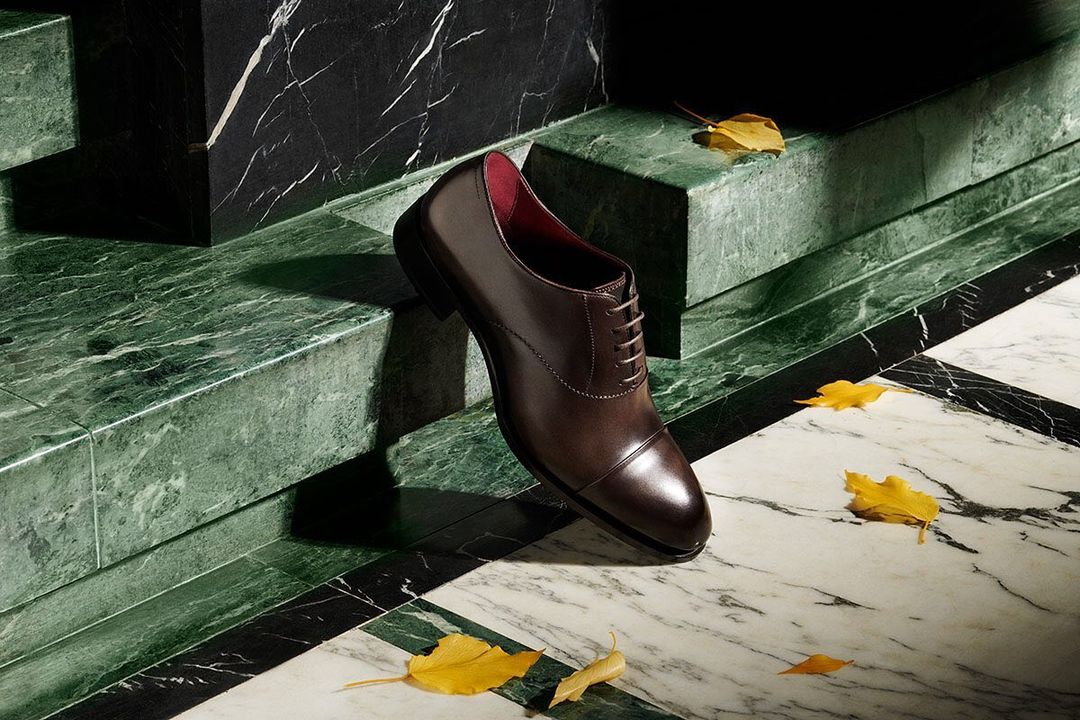 Elegant brown leather dress shoe showcased on marble steps with fallen autumn leaves, creating a sophisticated and seasonal aesthetic.