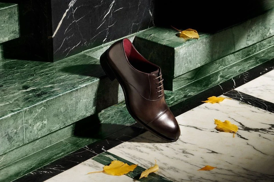 Elegant brown leather dress shoe showcased on marble steps with fallen autumn leaves, creating a sophisticated and seasonal aesthetic.