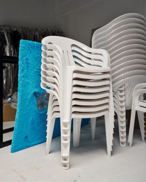 Stack of white plastic armchairs in a warehouse setting, showcasing modern furniture design and space-saving storage solutions.