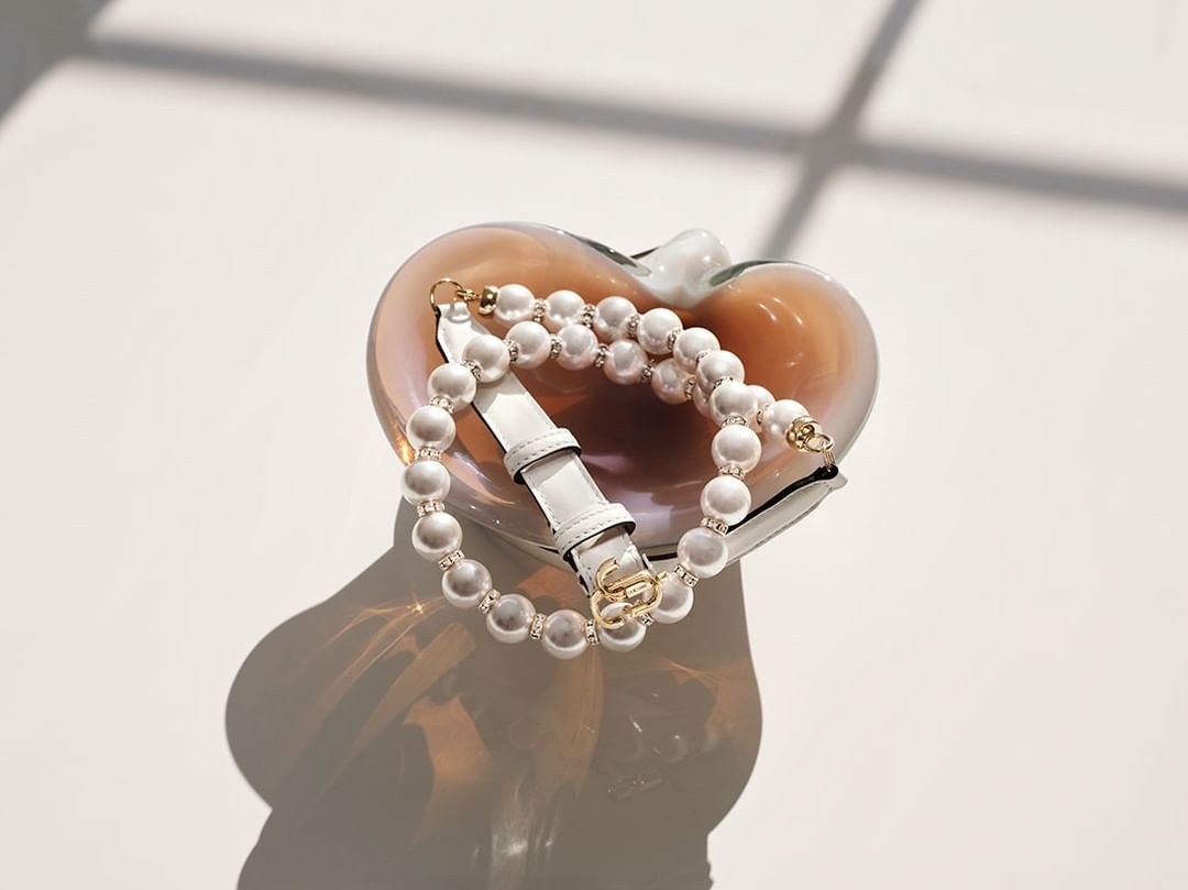 Elegant handbag with pearl strap in an art glass dish, casting shadows on a white surface, showcasing luxury fashion and accessories.