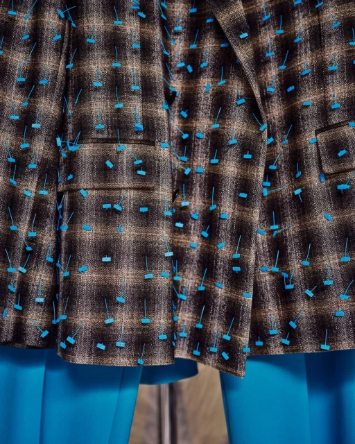 Close-up of a brown plaid jacket with unique turquoise embellishments and matching turquoise leggings, showcasing fashion design.