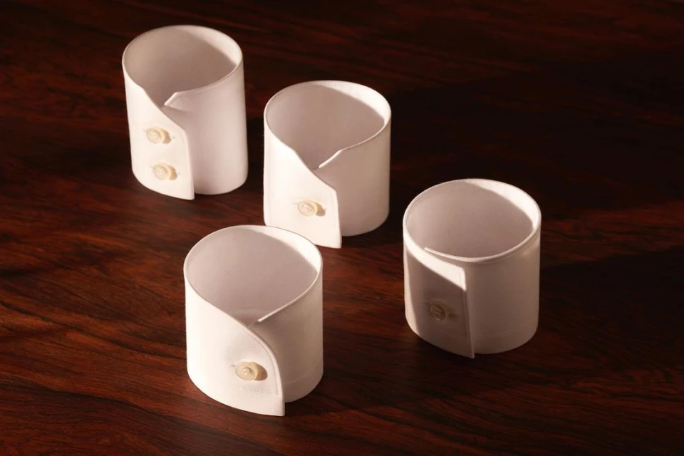 Four neatly arranged white shirt cuffs with button details are displayed on a dark wooden surface, creating a clean and minimalistic aesthetic.