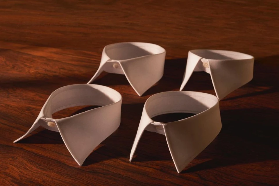 Four white dress shirt collars are neatly arranged on a polished wood surface, evenly lit to highlight their formal design.