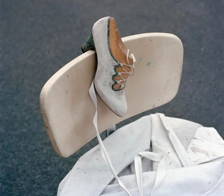 Still life of a high-heeled shoe with ribbons on a white chair outdoors, featuring a gray-blue background for a clean aesthetic.