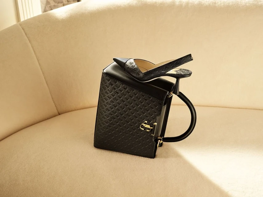 Elegant black purse and pointed-toe heel on a soft cream couch. Designer handbag and shoe pair fashion style, luxurious indoor setting.