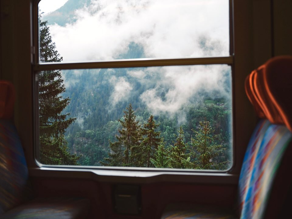 A view of forested mountains covered in mist through a train window, capturing the serene outdoor landscape.