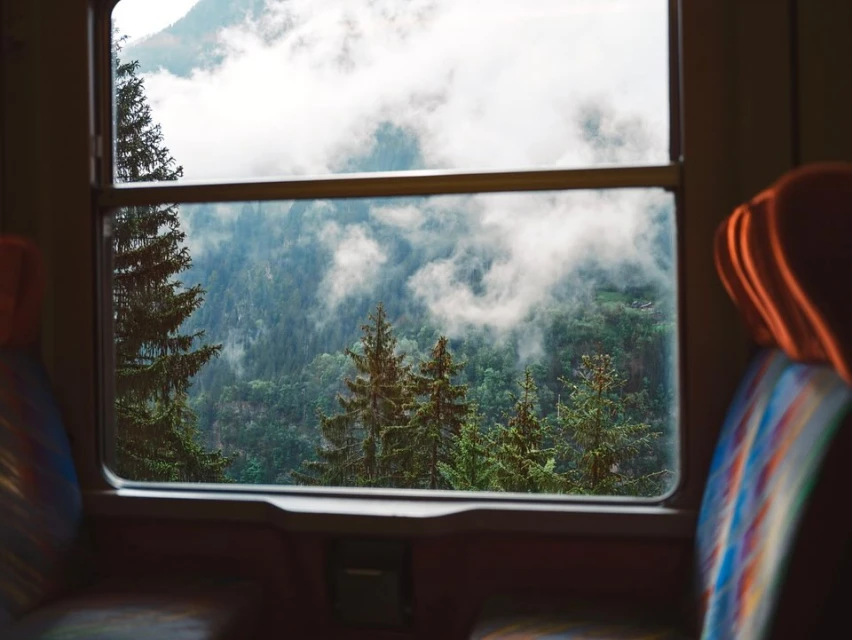 A view of forested mountains covered in mist through a train window, capturing the serene outdoor landscape.