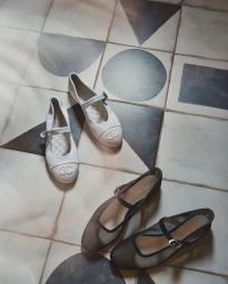 Two pairs of Mary Jane flats, one white and one dark, resting on a patterned tile floor with geometric shapes.