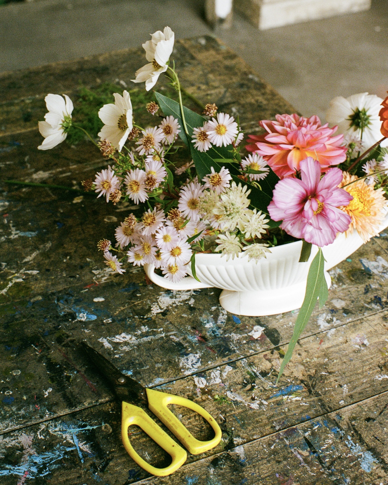 Floral arrangement in a white vase on a wooden table next to yellow handled scissors, capturing the essence of floral design.