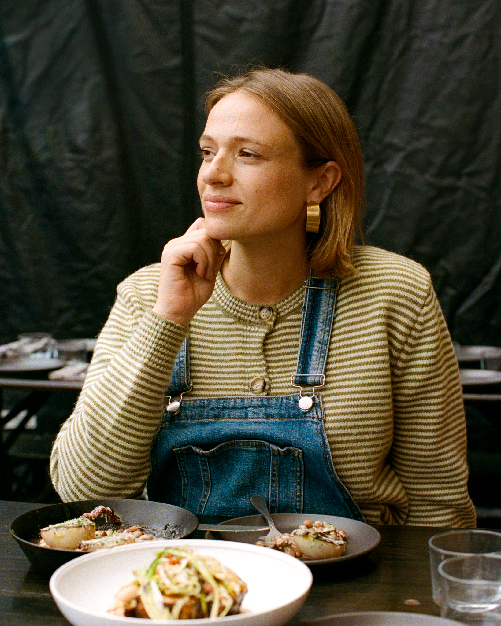 Portrait of a young adult female at a table in a restaurant or home, enjoying a meal with plates of prepared food and glassware.