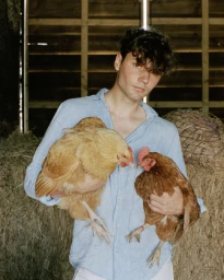 Young man holding two chickens in a rustic barn setting by photographer Aniella