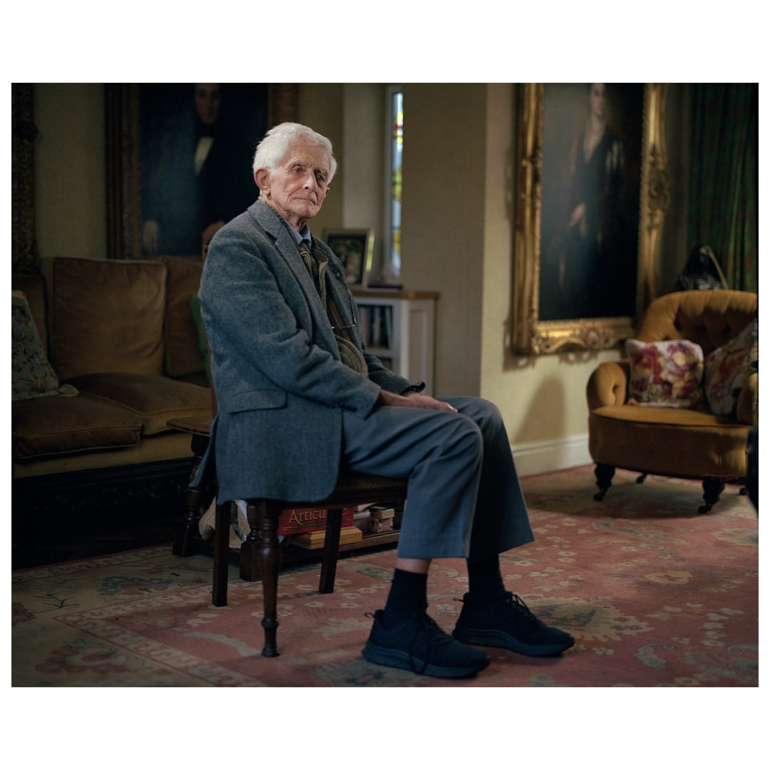 Elderly man in a grey suit jacket and trousers seated on a dark wooden chair in a living room by photographer Chris Floyd.