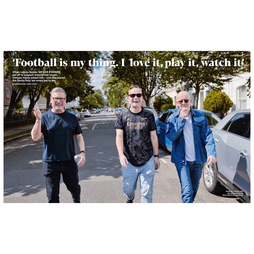 Three men walk down a residential street on a sunny day; one wears a soccer jersey, with cars and houses in the background.