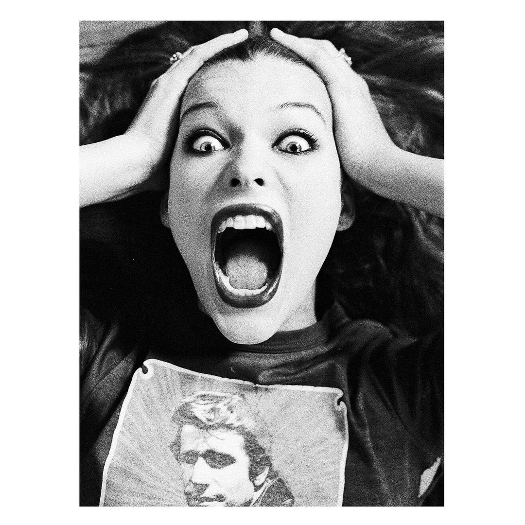 Black and white portrait of a woman screaming with her hands on her head, wearing a t-shirt with a portrait on it.