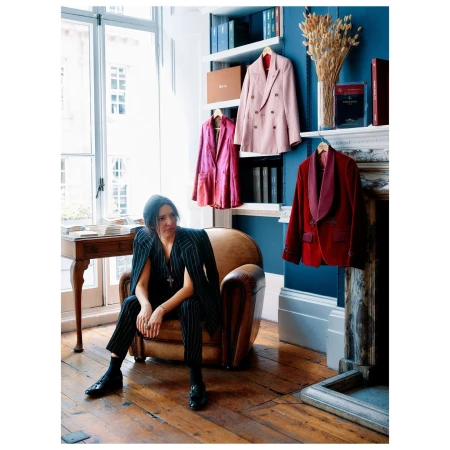 Woman in pinstripe suit sitting in leather armchair in room with blue walls and hanging blazers