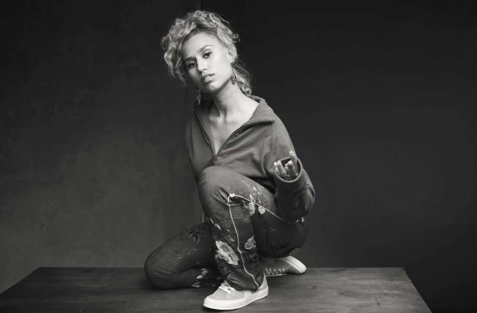 Monochrome portrait of a woman crouching on a dark wooden surface in a half-zip top and patterned pants, photographed by Chris Floyd.