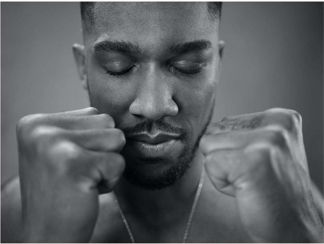 Black and white portrait of a contemplative adult male with eyes closed and fists clenched in front of a solid grey background.