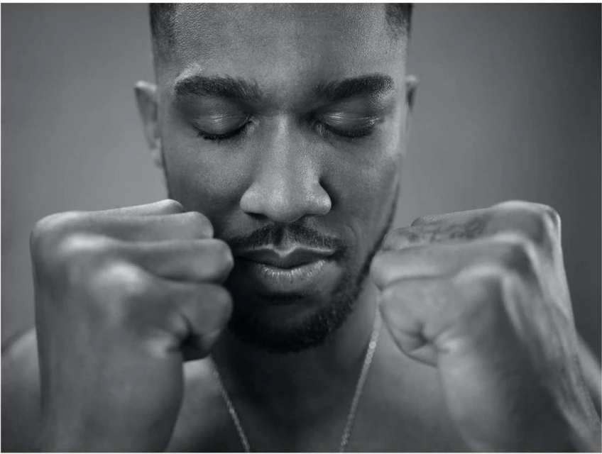 Black and white portrait of a contemplative adult male with eyes closed and fists clenched in front of a solid grey background.
