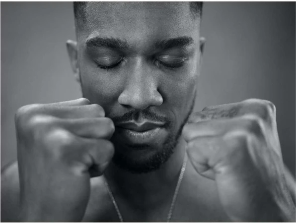 Black and white portrait of a contemplative adult male with eyes closed and fists clenched in front of a solid grey background.