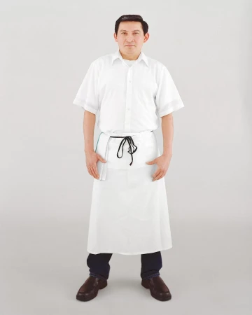 Full shot of a man in a white chef's uniform and apron, hands in pockets, posing against a light gray background in a studio setting.