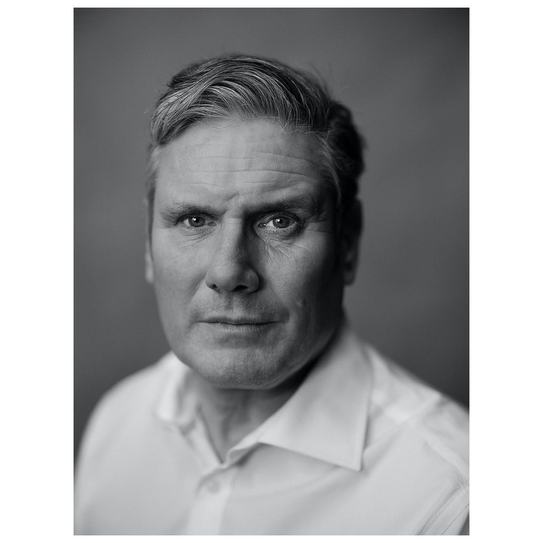 Monochrome portrait of a middle-aged man with graying hair, wearing a white collared shirt, set against a plain gray backdrop.