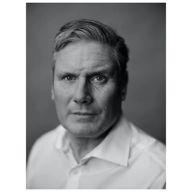 Monochrome portrait of a middle-aged man with graying hair, wearing a white collared shirt, set against a plain gray backdrop.