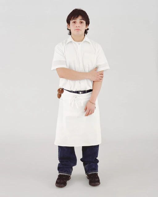 Full-shot studio portrait of a young adult male in a white cook's shirt and apron, dark jeans, with a neutral expression.