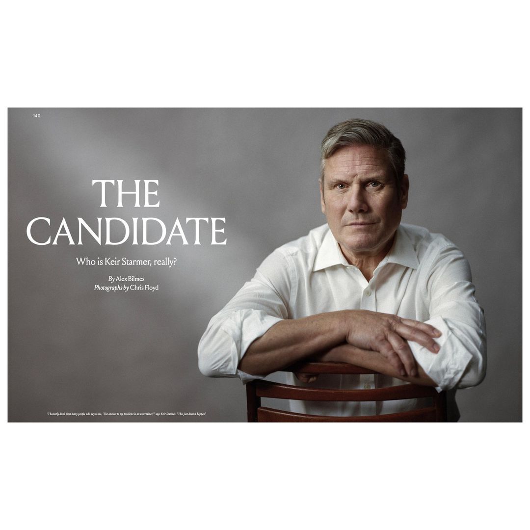 Portrait of a man in a white shirt sitting on a wooden chair against a grey backdrop, capturing a natural and slightly formal look.