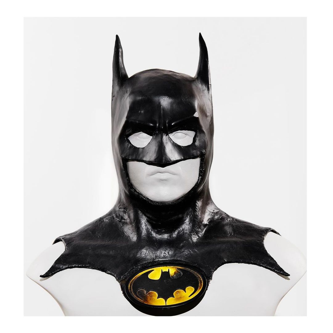 Batman cowl on a white mannequin against a white background, presenting the iconic logo with yellow and black.