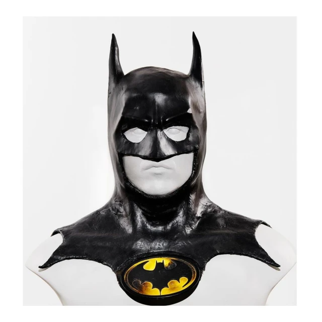 Batman cowl on a white mannequin against a white background, presenting the iconic logo with yellow and black.