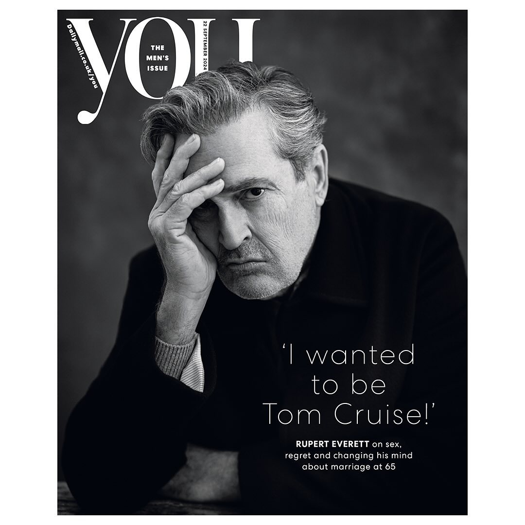 Black and white portrait of Rupert Everett on the cover of YOU magazine, looking thoughtful with his hand on his forehead.