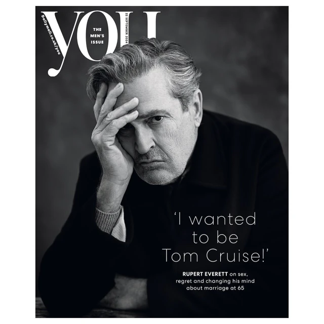 Black and white portrait of Rupert Everett on the cover of YOU magazine, looking thoughtful with his hand on his forehead.