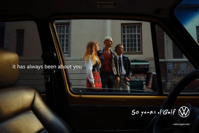 Vintage Volkswagen advert featuring three young people in front of a building viewed through the window of an old car.
