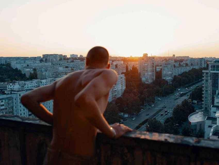 Adult male overlooking urban cityscape during golden hour. The background features high-rise buildings and a street with cars.