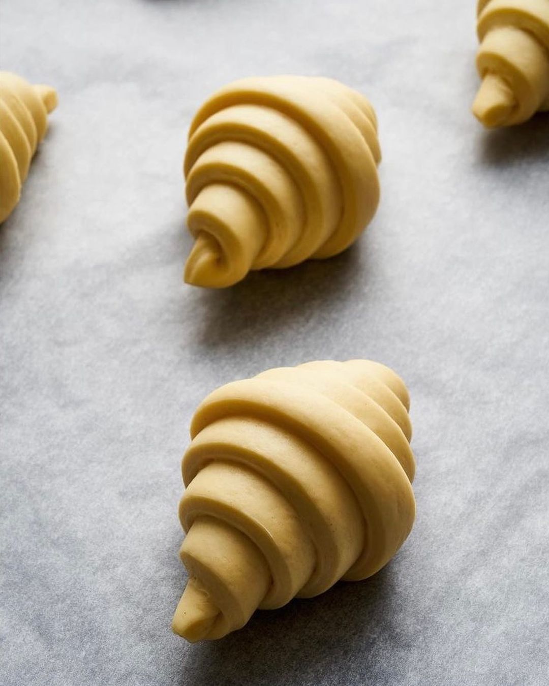 Close-up of several uncooked croissants lined up on a baking sheet covered with parchment paper, ready to be baked in the oven.