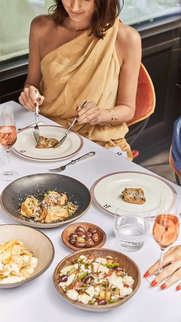 Overhead shot of a woman dining at a table with several dishes of food, drinks, and utensils in a restaurant setting.