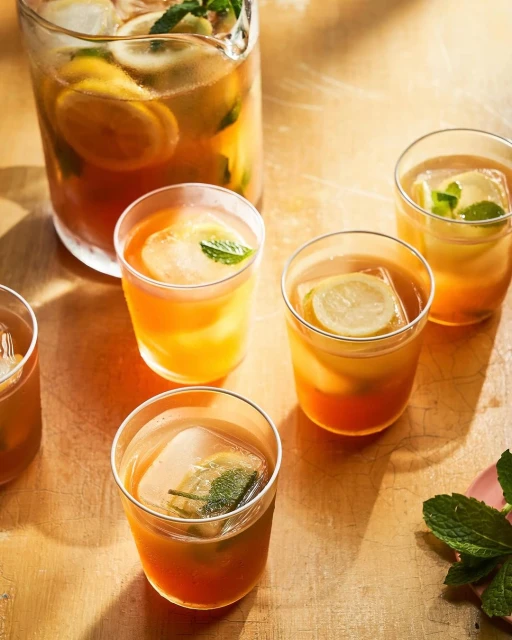 Refreshing iced tea in glasses and a pitcher features lemon slices and mint leaves, creating an inviting beverage composition.