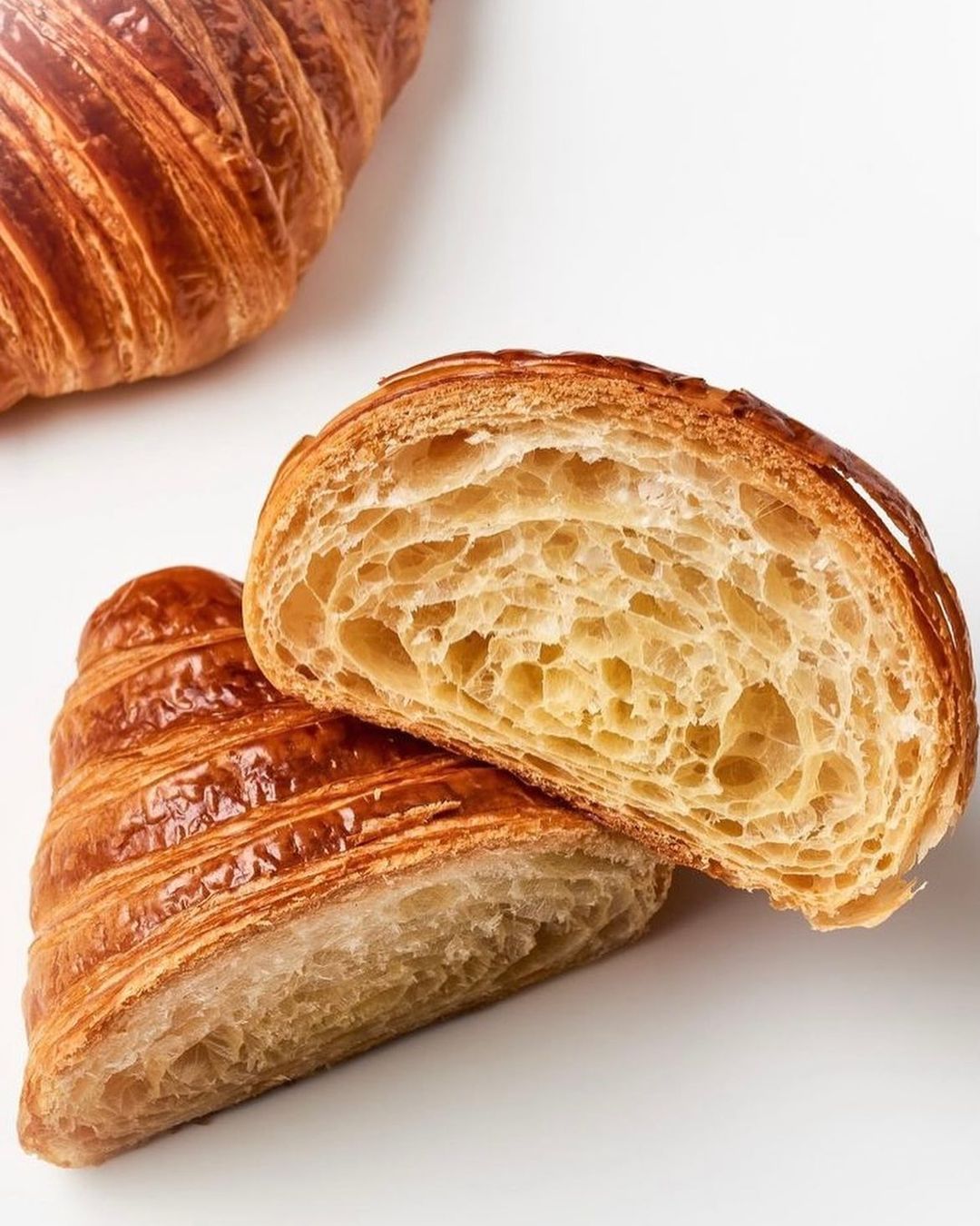 Overhead view of a sliced croissant with golden crust and airy interior, sitting on a white surface with another croissant in the background.