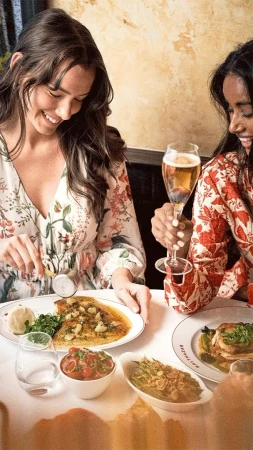 Two women enjoy lunch at a restaurant, sharing dishes and drinks. The focus is on food presentation and social dining in an indoor setting.