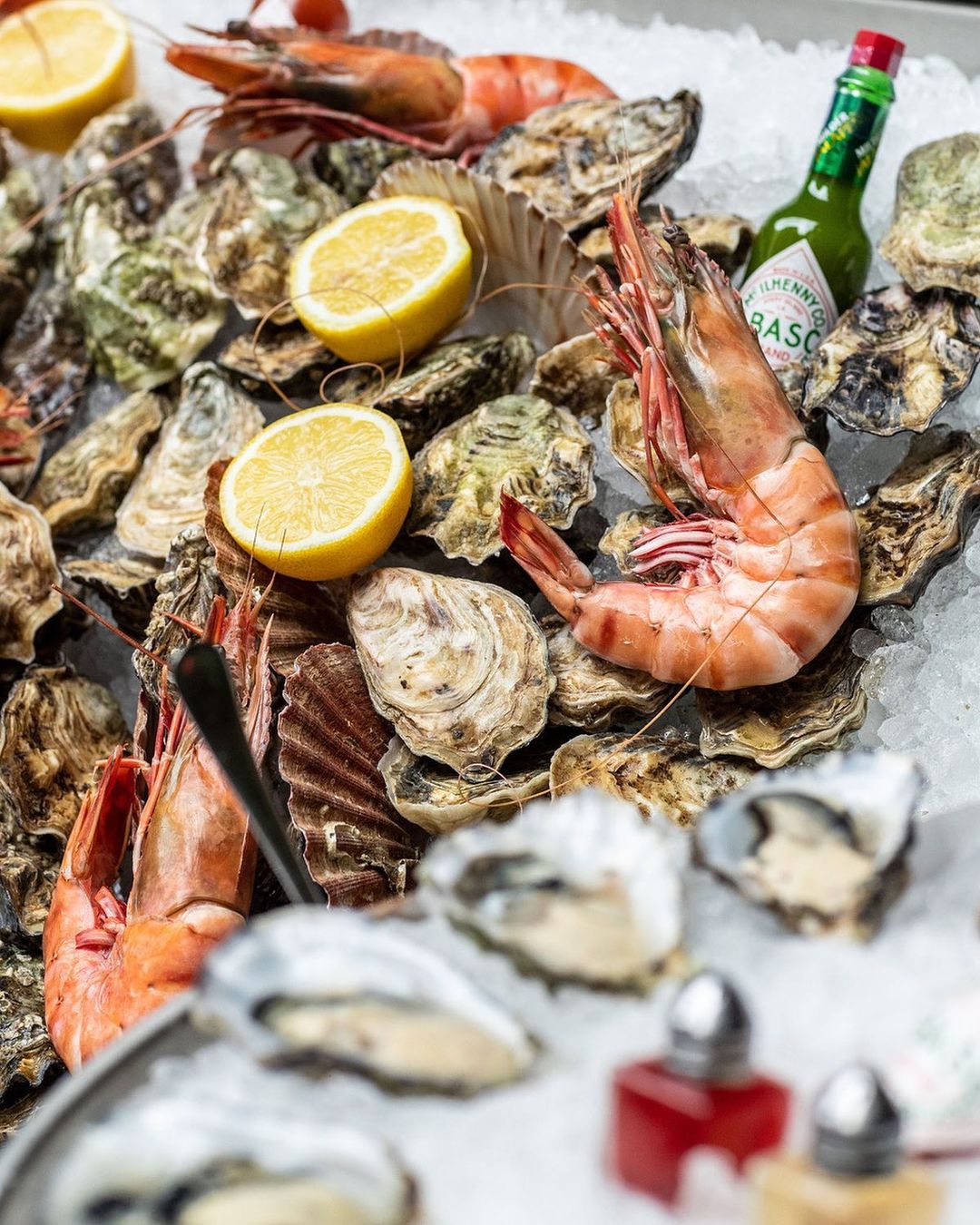 Overhead shot of fresh oysters, shrimp, lemon wedges, and Tabasco sauce served on crushed ice, food and beverage, studio lighting.