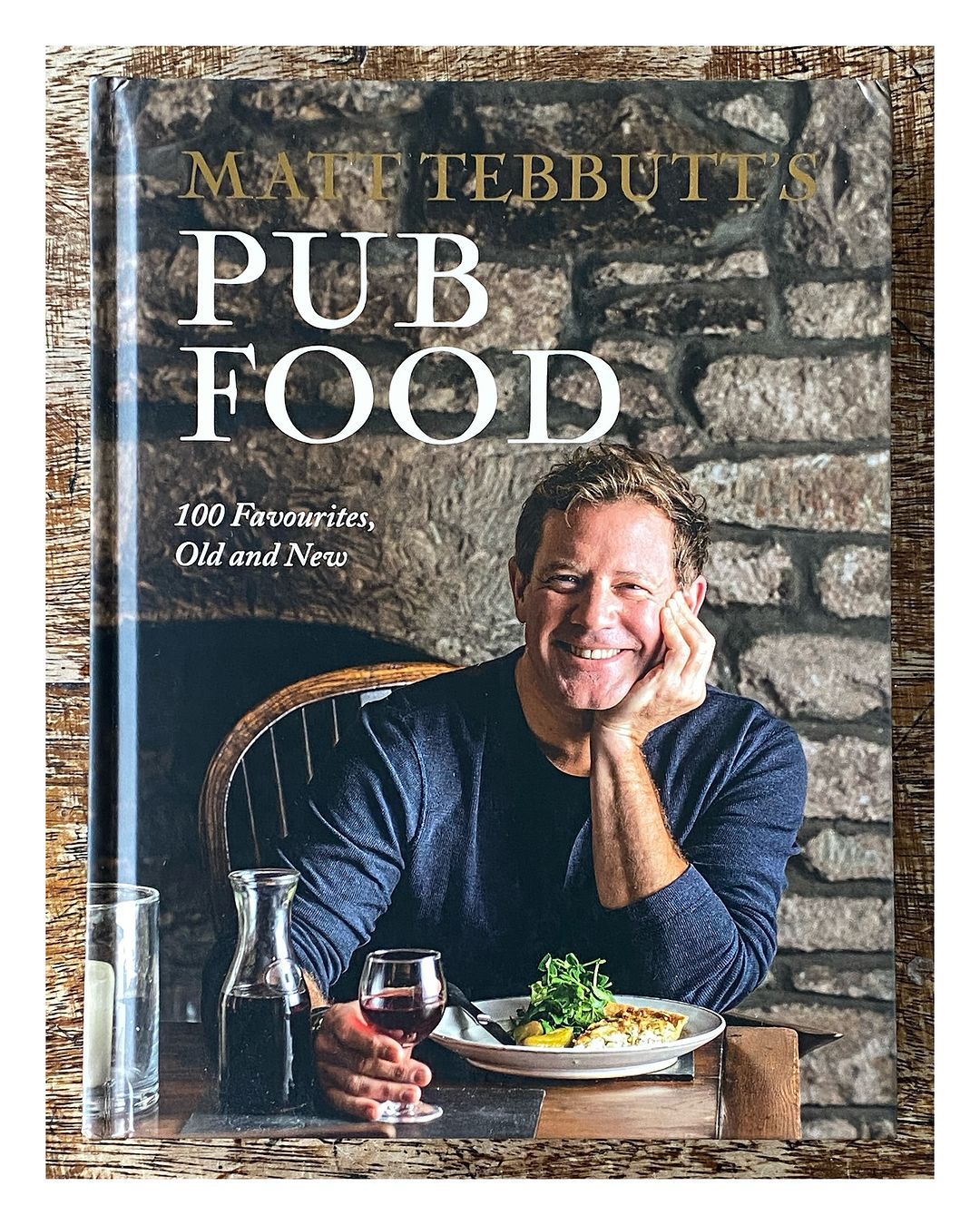 Book cover featuring chef Matt Tebbutt's cookbook 'Pub Food' against a stone wall, showcasing a smiling chef and a plate of food.