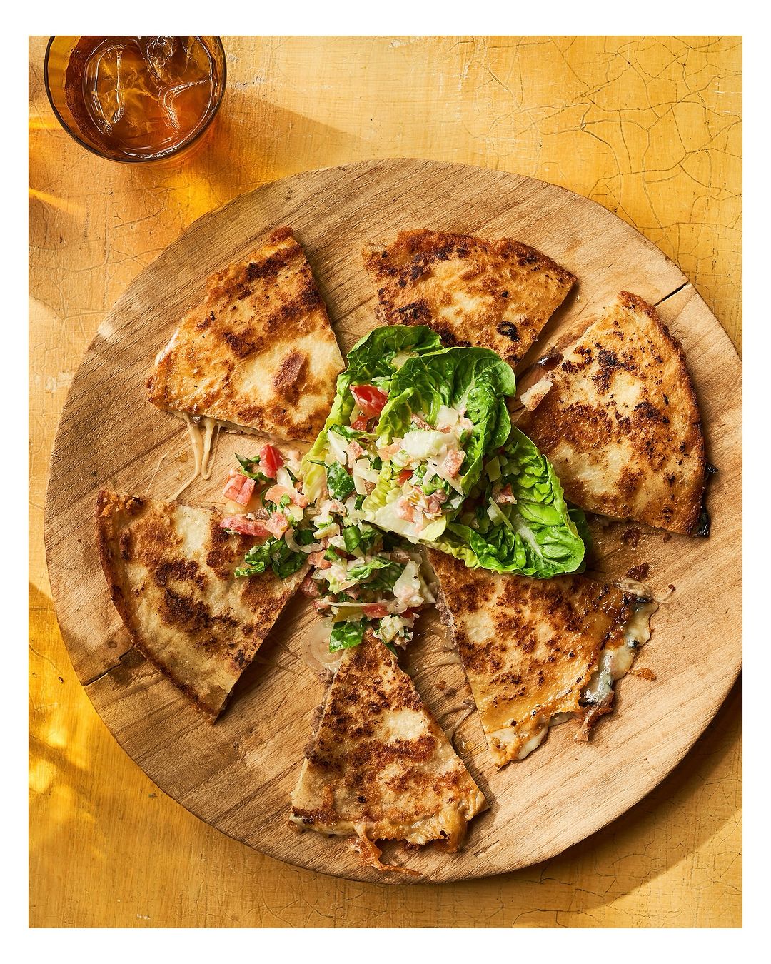 Overhead shot showcases quesadilla slices artfully arranged on a round wooden board with a side salad, creating a visually appealing food composition.
