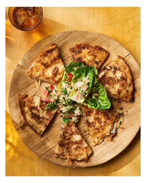Overhead shot showcases quesadilla slices artfully arranged on a round wooden board with a side salad, creating a visually appealing food composition.