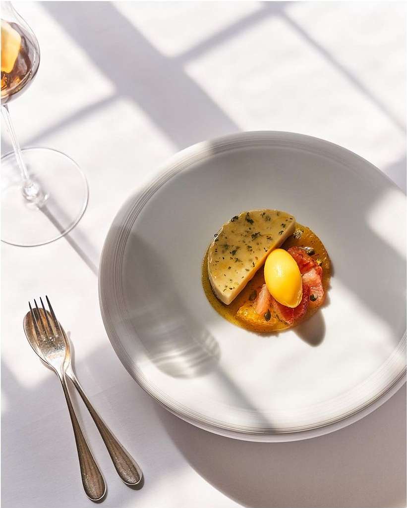 Elevated food photography showcases elegantly plated savory dessert with spherical garnish, silver cutlery, and a wine glass on a white table.